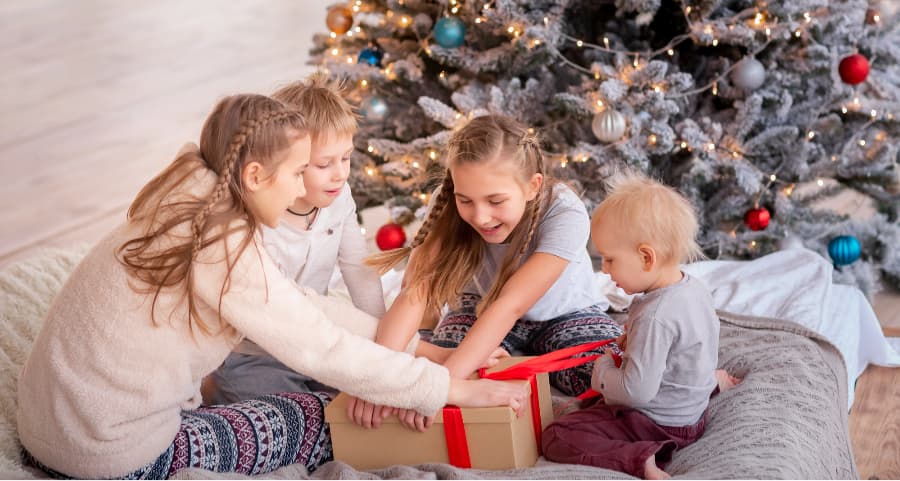 Children opening a present beside a Christmas tree.